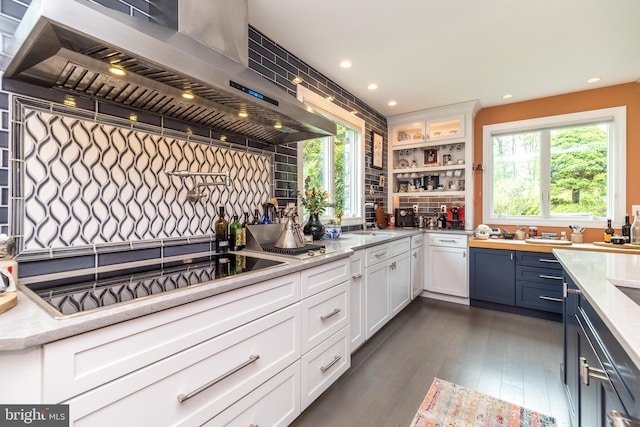 kitchen with wall chimney range hood, black electric stovetop, white cabinetry, and plenty of natural light
