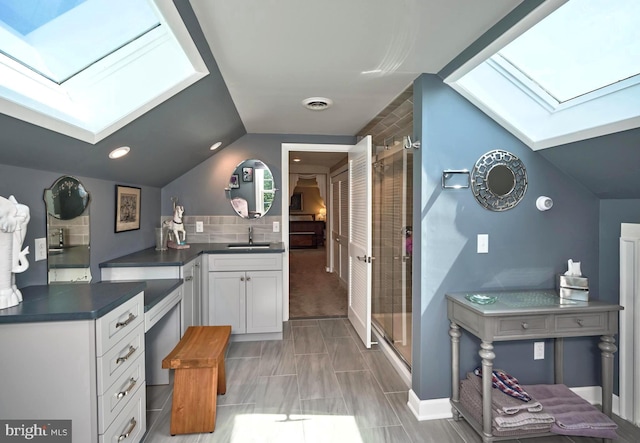 kitchen with a skylight, a sink, dark countertops, white cabinets, and lofted ceiling