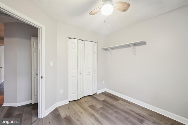 unfurnished bedroom featuring wood finished floors, baseboards, a closet, and ceiling fan