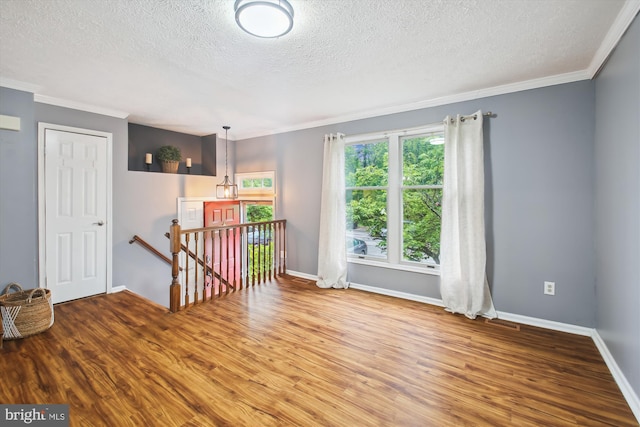 unfurnished room with a textured ceiling, wood finished floors, ornamental molding, and baseboards