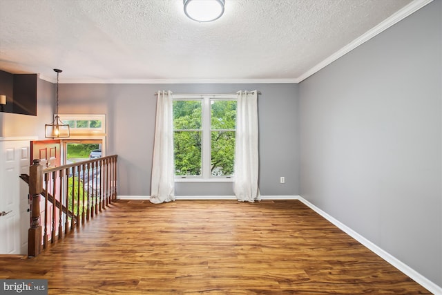 empty room with a textured ceiling, wood finished floors, crown molding, and baseboards