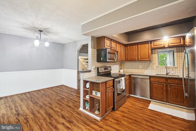 kitchen featuring appliances with stainless steel finishes, a sink, dark wood-type flooring, a textured ceiling, and light stone counters