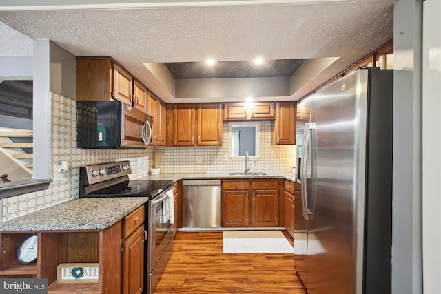 kitchen with appliances with stainless steel finishes, a sink, a textured ceiling, light wood-type flooring, and brown cabinets