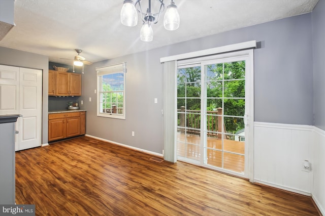 kitchen featuring brown cabinetry, wood finished floors, a chandelier, a ceiling fan, and baseboards