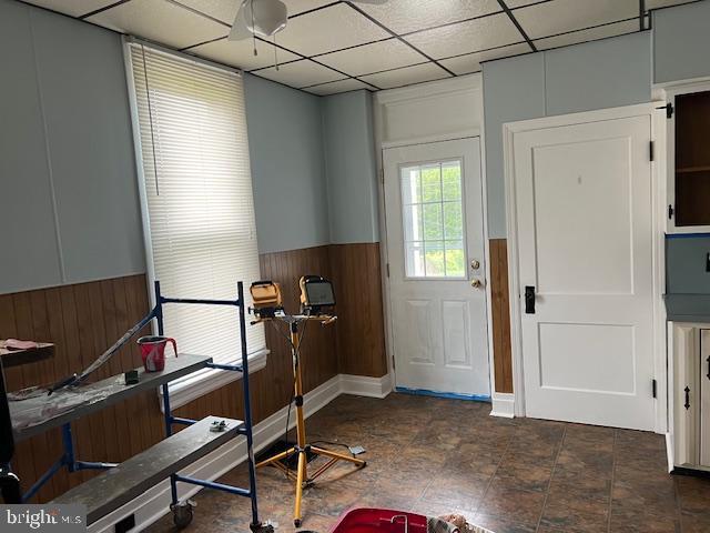 interior space with a wainscoted wall, wood walls, and a paneled ceiling