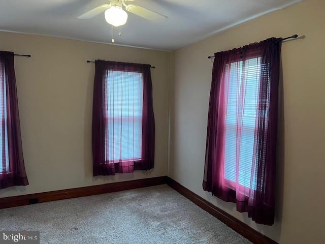 unfurnished room featuring a wealth of natural light, ceiling fan, carpet, and baseboards