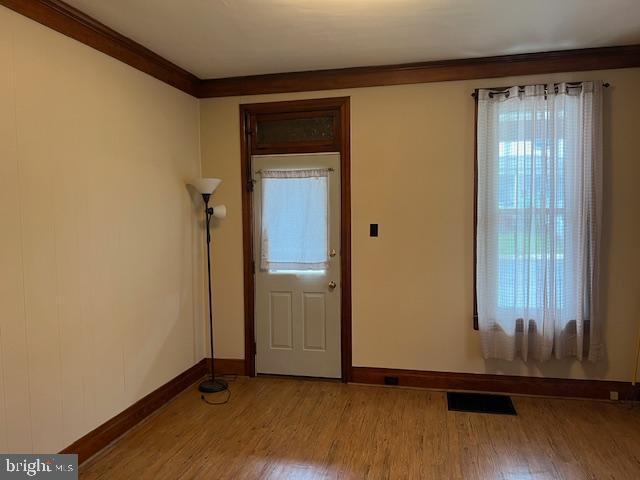doorway to outside featuring baseboards, visible vents, crown molding, and light wood finished floors