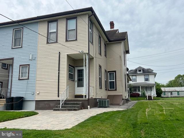 rear view of house featuring entry steps, a chimney, a patio area, a yard, and central AC