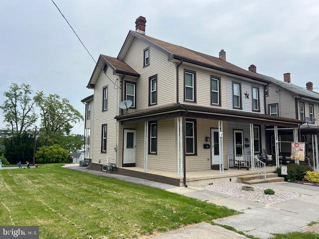 view of front facade featuring covered porch, a chimney, and a front lawn