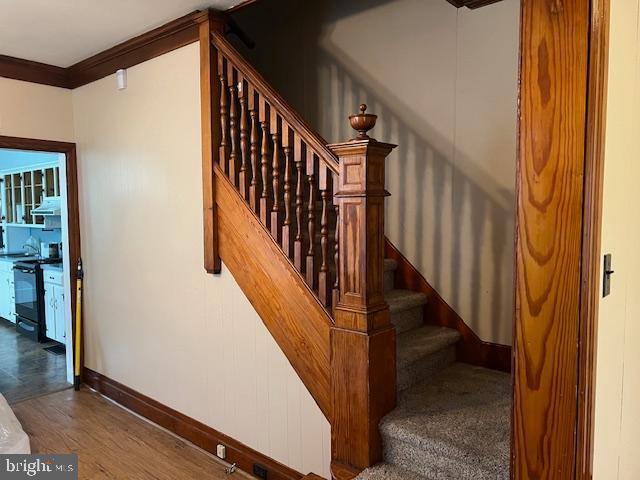 stairway with crown molding, wood finished floors, and baseboards