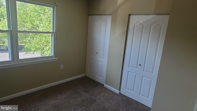 unfurnished bedroom with dark colored carpet, baseboards, and multiple windows