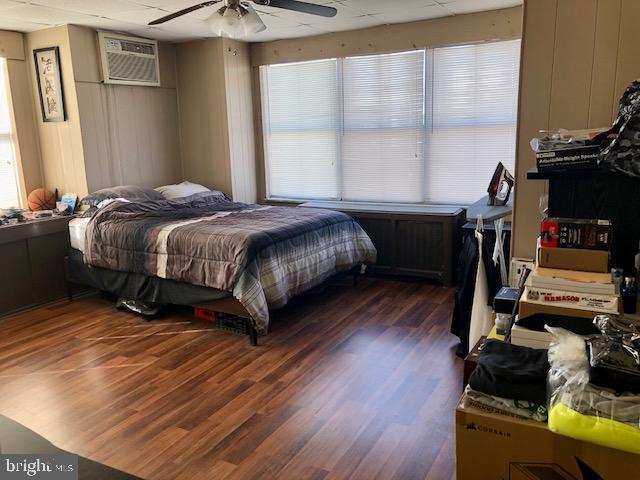 bedroom with an AC wall unit, a ceiling fan, and wood finished floors