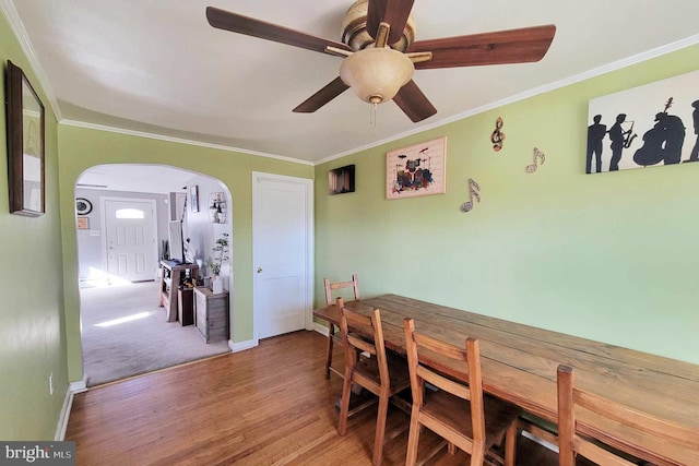 dining area with wood finished floors, arched walkways, ornamental molding, and ceiling fan