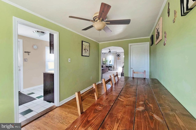unfurnished dining area featuring baseboards, ornamental molding, a ceiling fan, arched walkways, and wood finished floors