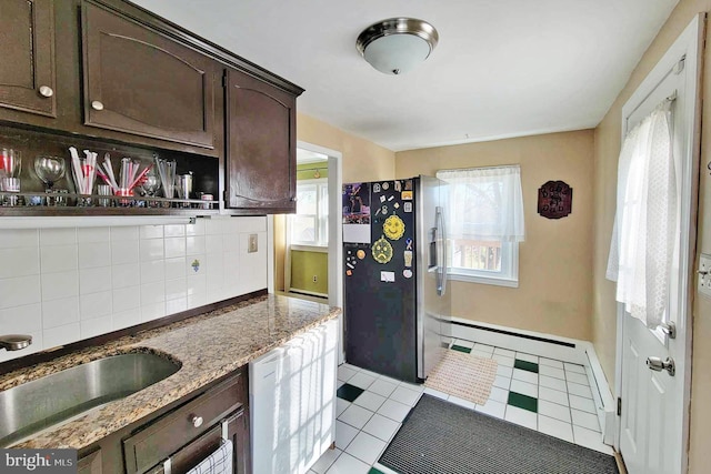 kitchen with tasteful backsplash, a sink, a wealth of natural light, freestanding refrigerator, and dark brown cabinets