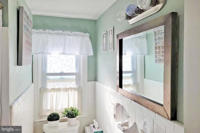 half bath featuring a wainscoted wall, tile walls, and toilet