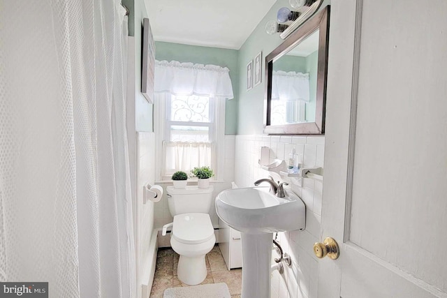bathroom with curtained shower, tile patterned flooring, toilet, wainscoting, and tile walls