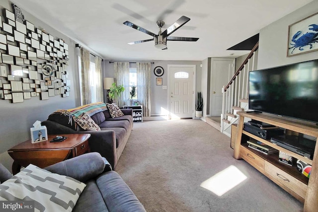 living area featuring baseboard heating, ceiling fan, carpet, and stairway