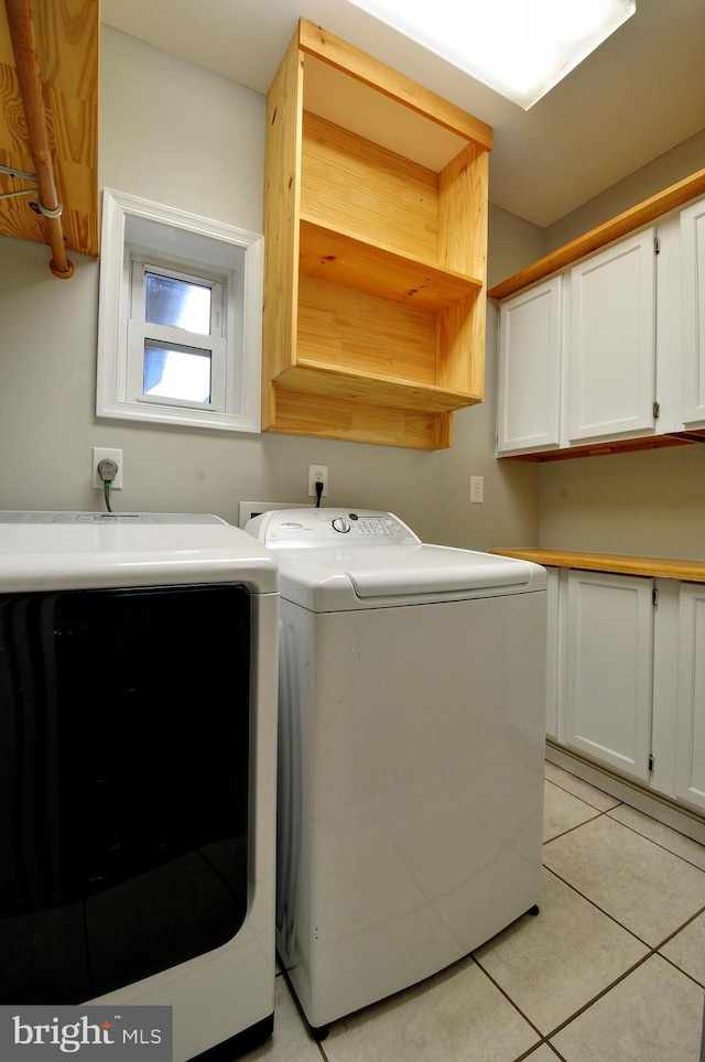 clothes washing area with cabinet space, washer and dryer, and light tile patterned floors