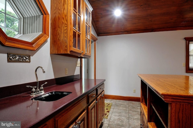 kitchen featuring a sink, light tile patterned flooring, dark countertops, baseboards, and glass insert cabinets