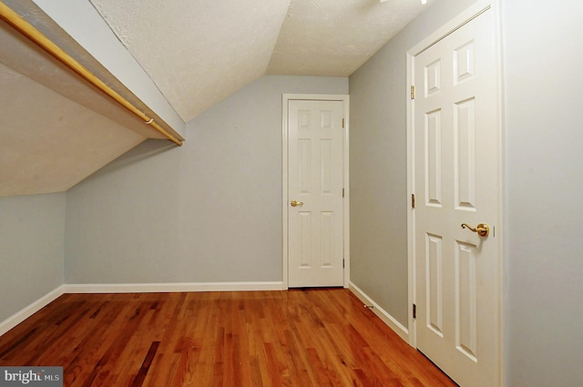 additional living space with light wood-type flooring, vaulted ceiling, baseboards, and a textured ceiling