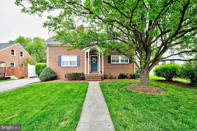view of front facade with brick siding, a front lawn, and fence