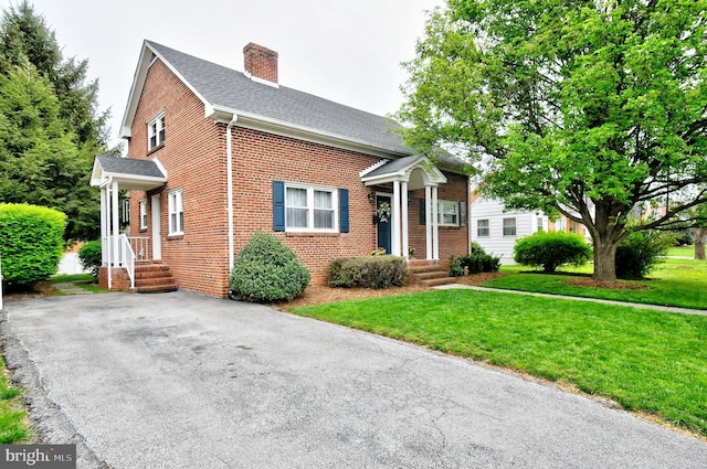 view of front of house featuring brick siding, roof with shingles, a chimney, and a front yard