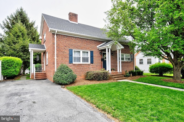 view of front of house with brick siding, roof with shingles, a chimney, and a front lawn