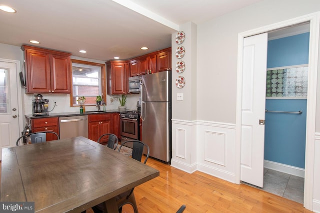 kitchen with recessed lighting, light wood-type flooring, stainless steel appliances, a sink, and dark countertops