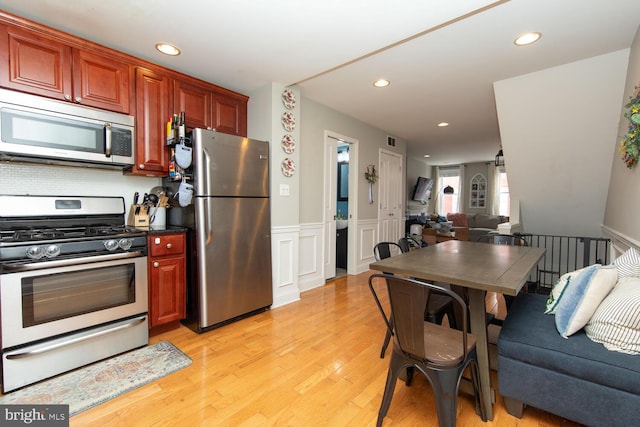 kitchen with a wainscoted wall, light wood finished floors, recessed lighting, appliances with stainless steel finishes, and open floor plan