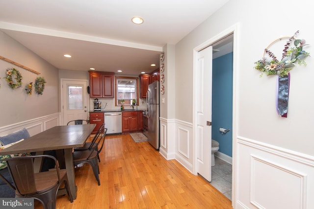 dining room featuring light wood-type flooring, a decorative wall, recessed lighting, and wainscoting