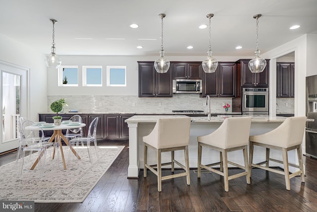 24642 Black Willow Dr, Aldie, VA 20105 - kitchen with appliances with stainless steel finishes, a kitchen island with sink, a breakfast bar area, and dark wood finished floors
