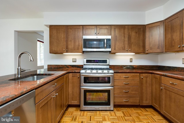 kitchen with dark stone counters, a sink, brown cabinets, and stainless steel appliances
