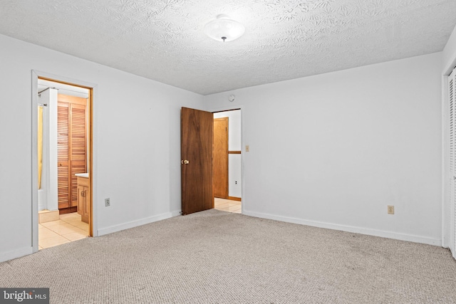unfurnished bedroom with light carpet, ensuite bath, baseboards, and a textured ceiling