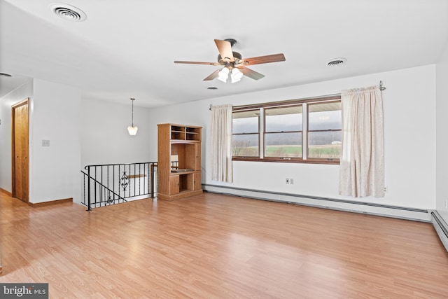 spare room with a baseboard radiator, light wood finished floors, ceiling fan, and visible vents