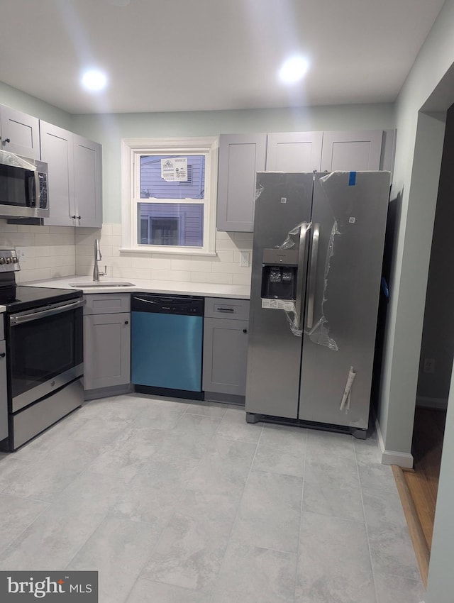 kitchen with gray cabinetry, a sink, stainless steel appliances, and backsplash