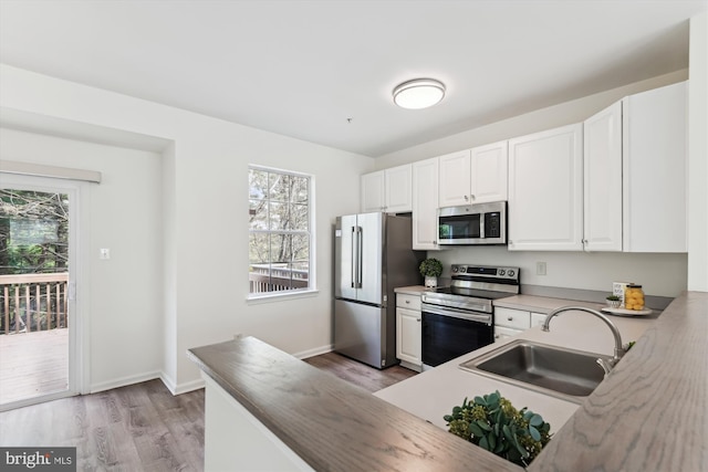 kitchen featuring light wood finished floors, a healthy amount of sunlight, appliances with stainless steel finishes, and a sink