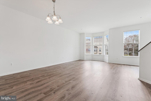 spare room with baseboards, wood finished floors, and an inviting chandelier
