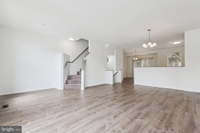 unfurnished living room featuring wood finished floors, visible vents, baseboards, a chandelier, and stairs