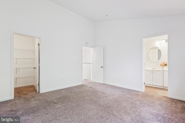 unfurnished bedroom with a walk in closet, light carpet, and baseboards