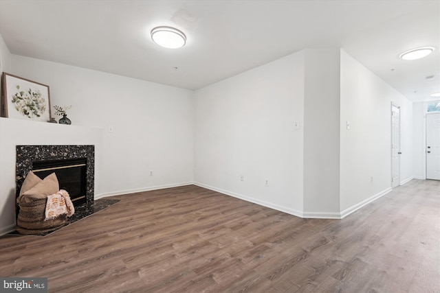 unfurnished living room featuring a premium fireplace, baseboards, and wood finished floors