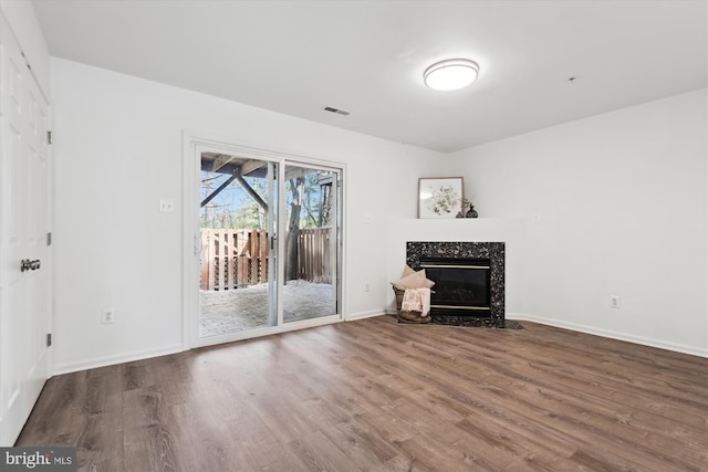 unfurnished living room featuring visible vents, a premium fireplace, baseboards, and wood finished floors