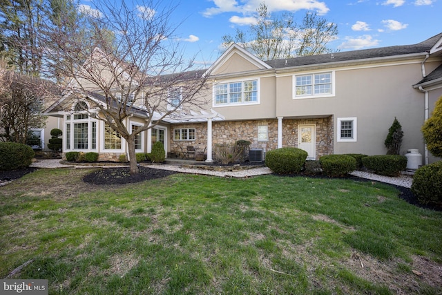 back of property with stucco siding, stone siding, a patio area, central AC unit, and a yard
