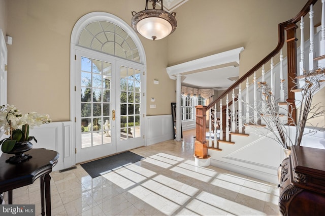 foyer entrance featuring a high ceiling, a decorative wall, wainscoting, stairs, and french doors