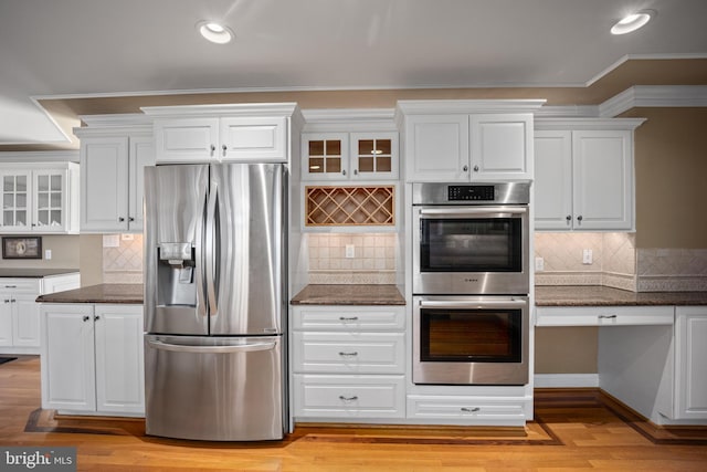 kitchen with stainless steel appliances, tasteful backsplash, glass insert cabinets, and white cabinetry