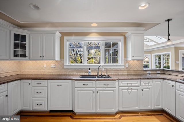 kitchen with glass insert cabinets, a sink, white cabinetry, pendant lighting, and a skylight