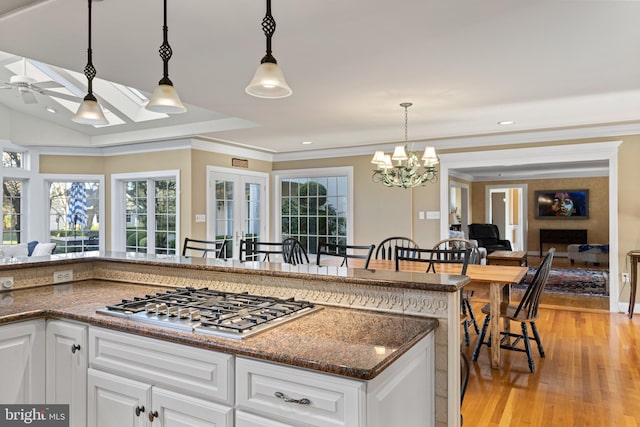 kitchen with stainless steel gas cooktop, ceiling fan with notable chandelier, light wood finished floors, and white cabinetry