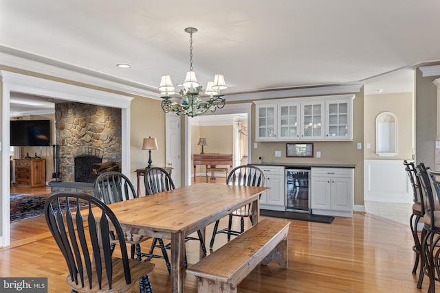 dining room featuring wine cooler, a notable chandelier, ornamental molding, and light wood-style floors