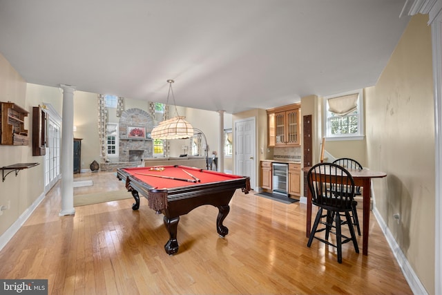 playroom with baseboards, a stone fireplace, light wood-type flooring, decorative columns, and beverage cooler