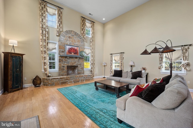 living area featuring visible vents, baseboards, hardwood / wood-style flooring, a fireplace, and a towering ceiling